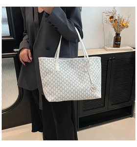 Close-up of white tote bag with M-letter print and metallic circular logo charm detail