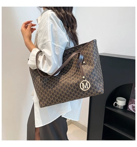 Close-up of letter print tote bag featuring a decorative metal M charm and sturdy handles