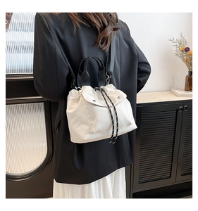 Detail of white drawstring bucket bag with black woven handle and metal buckle