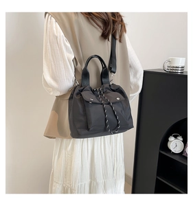 Detail of black nylon crossbody bag with dual snap pockets and woven drawstring closure