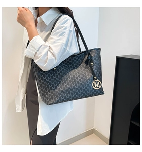 Detail of black monogram tote bag with repeat M pattern and golden logo pendant charm
