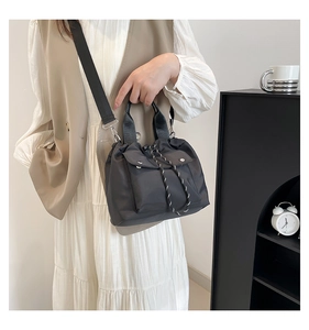 Detail of black nylon drawstring bucket bag with silver metal hardware and front flap pocket