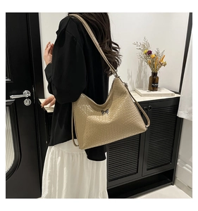 Detail of a beige woven hobo bag with metal bow buckle on a model in a home setting