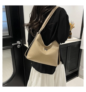 Detailed texture of beige woven hobo bag with a metal butterfly charm and long shoulder strap