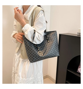 Detail of black tote bag with gray M pattern and metallic charm worn with beige outfit