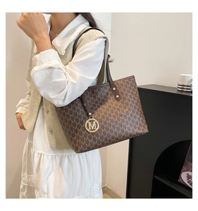 Detail of classic brown monogram tote bag with gold M-logo charm and slim shoulder straps