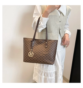 Detail view of brown tote bag with M-pattern monogram and metal logo pendant charm