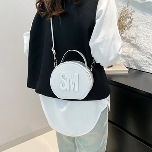 White round crossbody bag with SM embossed logo and top handle in a fashion portrait