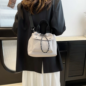 Minimalist light grey drawstring bucket bag with black strap worn over a black blazer