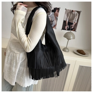 Detail of soft black faux leather tote with long fringe tassels shown on a model's shoulder