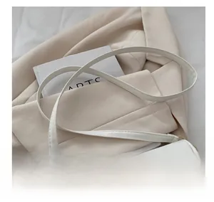 Detail of white leather crossbody bag showing golden irregular buckle and slim strap