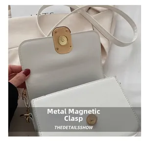 Close-up of golden oval magnetic buckle and white PU leather texture on a flap bag