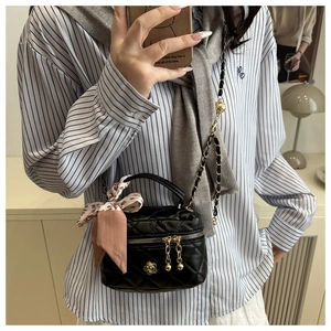 Close-up of black quilted mini bucket bag with gold camellia charm and silk scarf
