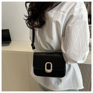 Detail view of a black crossbody square bag with a golden oval buckle and matte leather texture