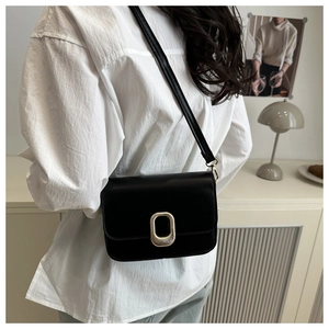 Detail of a black leather crossbody bag with a large oval gold metal buckle clasp