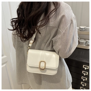 Detail of white leather crossbody bag with golden buckle shown on a model's shoulder