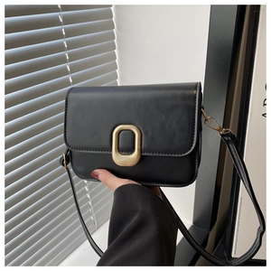 Close-up of black leather crossbody bag with oval gold embossed metal buckle detail