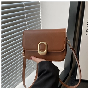 Detail of a brown leather crossbody bag with an oval gold buckle and flap design