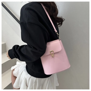 Detail of light pink glossy leather bucket bag with gold buckle on a shoulder strap