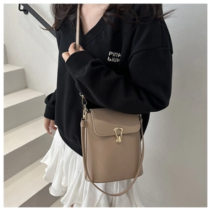Fashionable beige leather crossbody bag with gold buckle worn by model on stairs