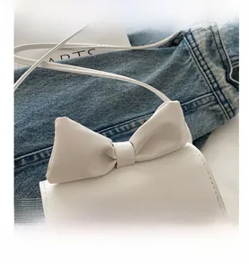Détail d'un mini sac blanc avec nœud en cuir et logo doré posé sur un vêtement en jean