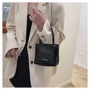 Détail du sac à main noir brillant avec logo sur mannequin en costume beige chic