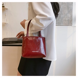 Détail d'un sac à main bordeaux en cuir verni avec logo tenu par un mannequin