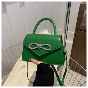 Detail of green crossbody bag with V-shaped flap and sparkling silver rhinestone bow charm