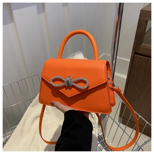 Close-up of orange leather handbag with sparkling silver rhinestone bow and top handle