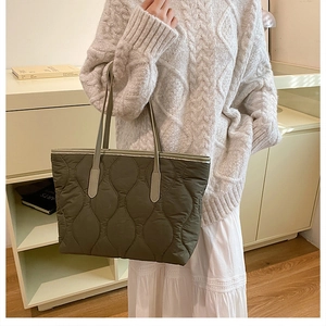 Model wearing a large olive green quilted tote bag with wavy stitching and slim straps