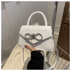 Close-up of white leather handbag featuring a sparkling rhinestone bow and top handle