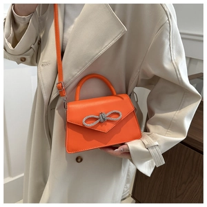 Detail of a bright orange mini handbag with a sparkling silver rhinestone bow decoration
