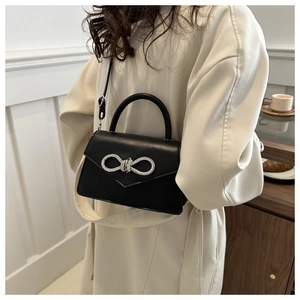 Detail of black crossbody bag featuring a sparkling rhinestone bow buckle and leather texture