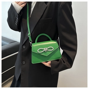 Detail of green crossbody bag featuring a silver rhinestone bow buckle and top handle