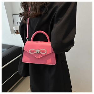 Bright pink crossbody bag with a sparkling diamond bow and detachable strap shown on model