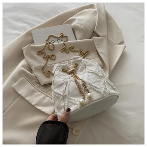 Close-up of white denim bucket bag with quilted texture, gold chain and pearl drawstring