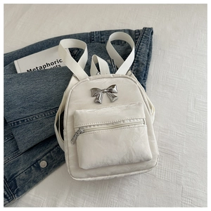 Détail d'un sac à dos blanc crème texturé avec un nœud métallique et de larges bretelles