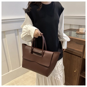 Detail of large dark brown tote bag showing elegant cylinder handles and flap design