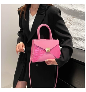 Detail of pink crossbody bag with crocodile texture, gold square buckle, and top handle