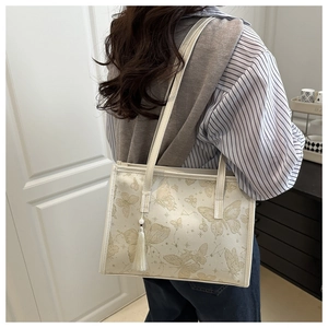 Détail d'un sac cabas blanc avec motifs papillons dorés et accessoire à pompon en soie