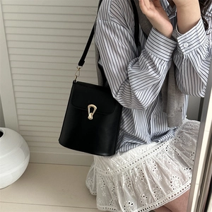 Classic black leather bucket bag with gold U-shaped buckle worn by a model in casual style