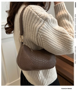 Detail of brown crocodile pattern shoulder bag with gold hardware on casual sweater