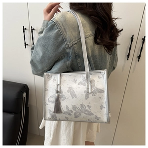 Détail du sac cabas argenté avec imprimé papillon gris et breloque à pompon en soie