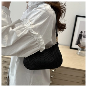 Detail of minimalist black faux snake skin texture on shoulder bag with gold metal hardware