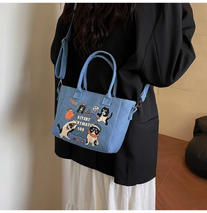 Detail of light blue denim tote featuring playful cartoon cat prints and metal hardware