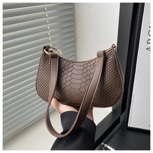 Dettaglio della texture in pelle di coccodrillo marrone e anelli dorati su borsa a spalla