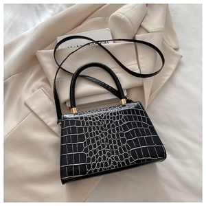 Detail of black faux leather handbag with white crocodile texture and gold hardware