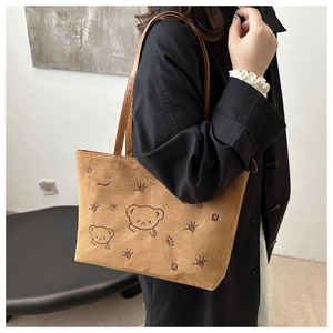 Close-up of brown suede tote bag with cartoon bear embroidery and soft leather straps