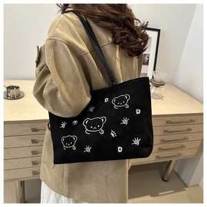 Close-up of a black canvas tote bag with white cartoon bear embroidery worn over a coat