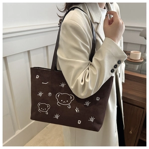 Detail of dark brown tote bag with white bear embroidery and black leather strap